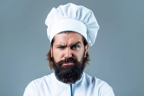Confident bearded male chef in white uniform. Serious cook in white uniform, chef hat. Portrait of a serious chef cook. Bearded chef, cooks or baker. Bearded male chefs isolated. Cook hat