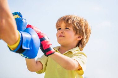 Baba oğlunu boks eğitiyor. Küçük çocuk büyükbabasıyla boks egzersizi yapıyor. Koçla boks antrenmanında küçük bir çocuk. Sporcu adam kırmızı boks eldivenli küçük çocuğa koçluk yapıyor.