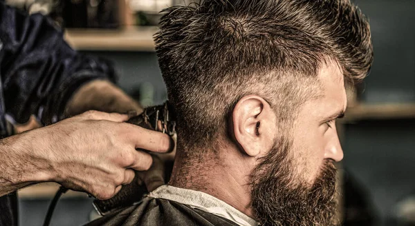 Conceito de corte de cabelo. Homem visitando cabeleireiro na barbearia. Barbeiro trabalha com cortador de cabelo. Um cliente Hipster a cortar o cabelo. Mãos de barbeiro com cortador de cabelo, close-up — Fotografia de Stock
