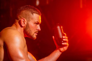 Genç adam spor salonunda su içer. Spor salonunda elinde su şişesi olan bir adam. Spor salonunda su içen yakışıklı kaslı adamın yaşam tarzı portresi. Kaslı adam su içiyor. Şişede su var.