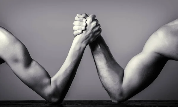 Two mans hands clasped arm wrestling, strong and weak, unequal match. Arm wrestling. Heavily muscled man arm wrestling a puny weak man. Black and white Stock Image