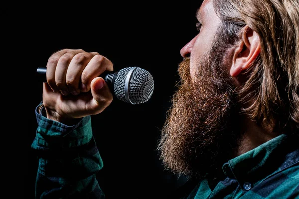 Male singing with a microphones. Man with a beard holding a microphone and singing. Bearded man in karaoke sings a song into a microphone. Male attends karaoke — Stock Photo, Image