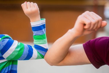 Baba ve oğul dirseklerini dışarıda çarpıştırıyor. Coronavirus karantinası. Sosyal uzaklık kavramı. Coronavirüs salgını. Koruyucu önlemler. Maskeli arkadaşlar, dirseklerinizi vurun.