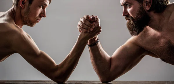 Two mans hands clasped arm wrestling, strong and weak, unequal match. Heavily muscled bearded man arm wrestling a puny weak man