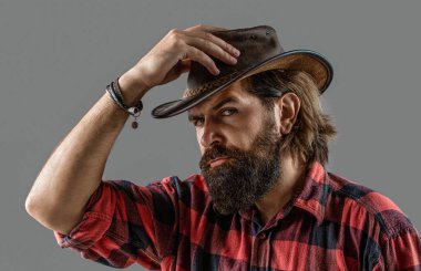 Deri kovboy şapkası. Kovboy şapkasını ayarlayan yakışıklı genç adam. Tıraşsız kovboylar. Amerikan kovboyu. Ekose gömlekli kovboy tarzı..