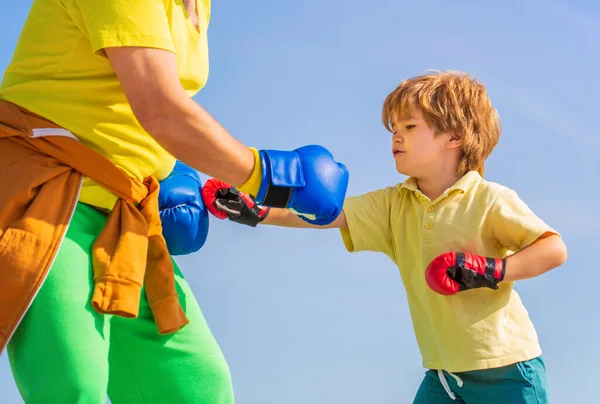 Adam oğlunu boks eğitiyor. Büyükbaba çocuk boks pozisyonunda duruyor. Dövüşçü. Kırmızı boks eldivenli küçük çocuğa koçluk yapan bir adam. Boks yapan küçük çocuk. Egzersiz yapıyor..