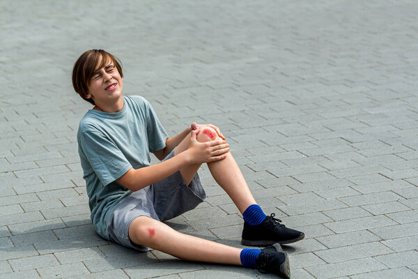 Unhappy child boy injured leg pain. Boy worried about leg injury in road. Child injured his knee when he fell. Blood and scratched skin. Young boy holding his injured knee.