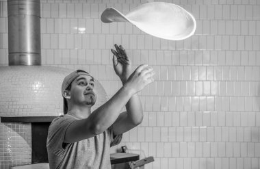 Becerikli şef pizzaya hamur hazırlıyor, elleriyle yuvarlanıyor ve kusuyor. Siyah ve beyaz.