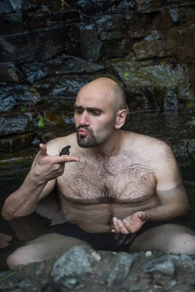 A young man takes a wild bath in a mineral spring in the taiga. Frogs also like healing water.