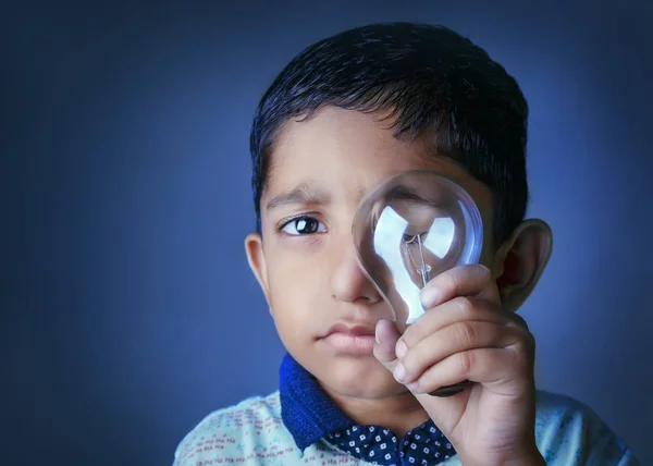Save Energy- Creative Portrait of little cute asian indian boy child holding bulb in hands with bokeh background closeup shot looking at camera