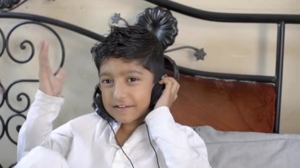 印度亚洲白人男孩与眼镜听耳机享受音乐微笑手上下跳舞点头在客厅室内看相机前视图 — 图库视频影像