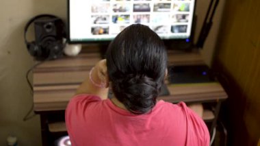 Çene üzerinde masaüstü pc el üzerinde çalışan pembe t-shirt Hint asya kafkas kadın. Ev hanımı masaüstü ekranında okuma internet sitesi blogu tarama. Yakın arka açılı üst görünüm kapalı çekim.   