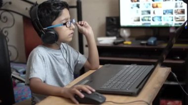 Hint Aisan Kafkas geeky oğlan çalışan üzerinde laptop giyen Kulaklık dinleme müzik. Arka planda müzik sevgilisi yan görünüm masaüstü ekran portresi. 