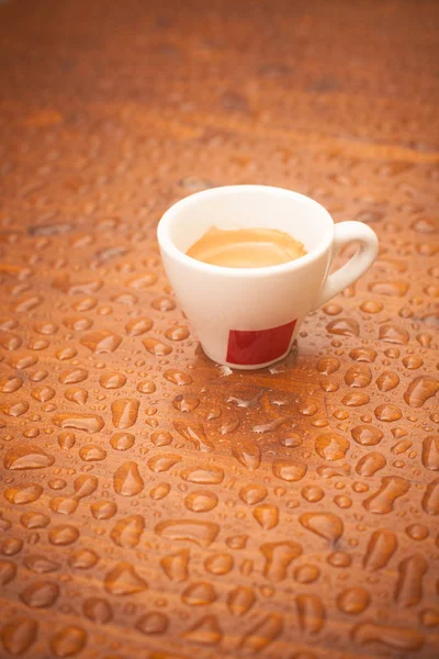A coffee cup on a wooden platform with rain drops.