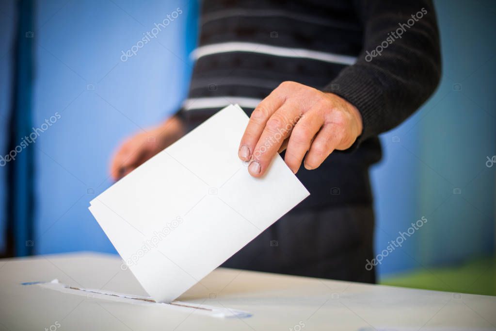 Color image of a person casting a ballot at a polling station, during elections.