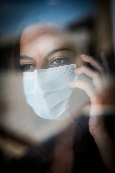 마스크를 창문으로 휴대폰으로 이야기하는 여자의 — 스톡 사진