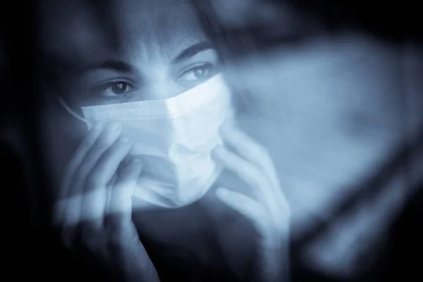 窓辺に外科用マスクをした女性の姿 — ストック写真