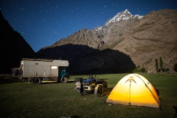 A motorhome, a sidecar motorcycle and a tent, camping at night in the mountains.