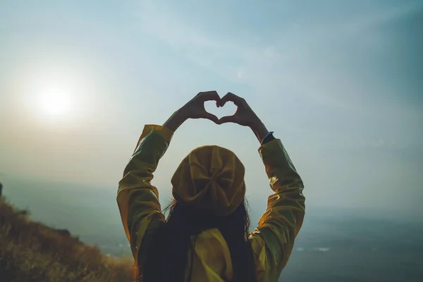 Uma jovem fazendo símbolo de coração com as mãos ao pôr do sol — Fotografia de Stock