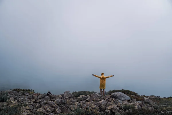 Θηλυκό σε κίτρινα αδιάβροχα, τζιν σορτς στέκεται στην κορυφή του βουνού με θέα των κορυφών στο horizon. Τοπίο. Φύση. — Φωτογραφία Αρχείου