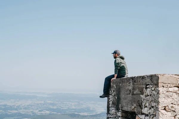 Άνθρωπος με καπάκι καθιστός πίσω κοιτάζοντας θέα από την κορυφή του κτιρίου. — Φωτογραφία Αρχείου