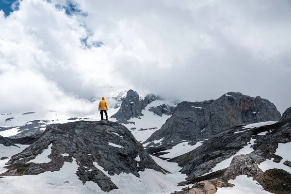 Männlicher Wanderer mit gelbem Regenmantel steht auf dem Gipfel des Berges. — Stockfoto