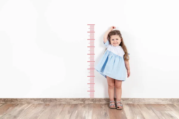 Niña rubia midiendo altura en pared blanca . — Foto de Stock