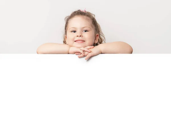 Sonriente niña de ojos azules asomándose detrás de una pizarra blanca —  Fotos de Stock