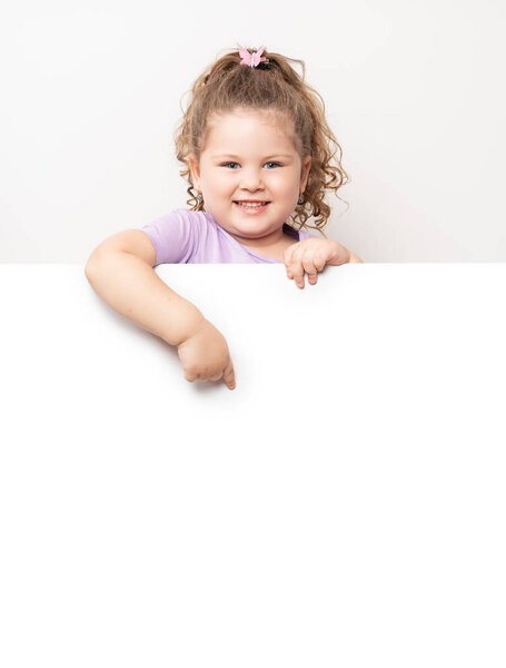 Smiling blue eyed little girl peeking behind a white board