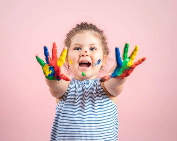 Lächelndes kleines Mädchen mit Händen in der Farbe auf rosa Hintergrund — Stockfoto