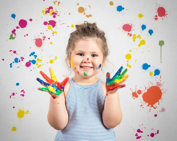 Усміхнена маленька дівчинка з руками в фарбі на пофарбованому фоні стіни . — стокове фото