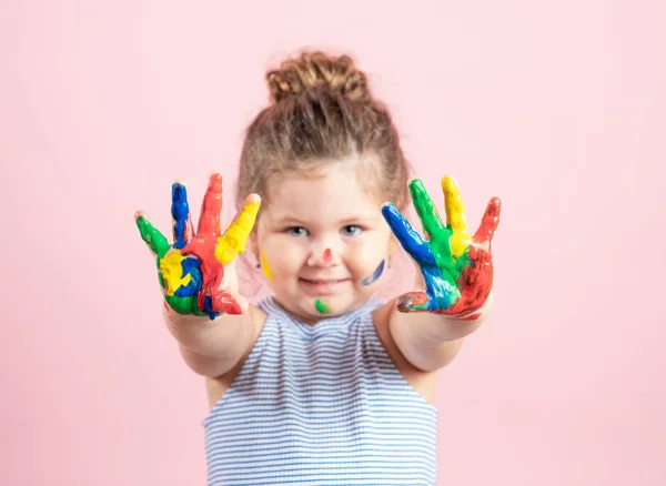 Lächelndes kleines Mädchen mit Händen in der Farbe auf rosa Hintergrund — Stockfoto