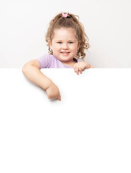 Smiling blue eyed little girl peeking behind a white board Stock Picture