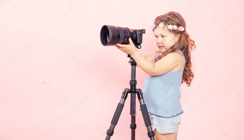 Little girl holding camera and smiling on pink background