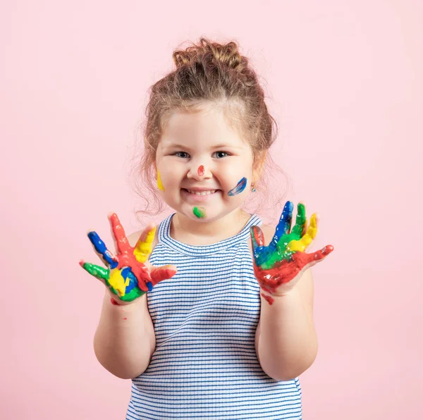 Niña sonriente con las manos en la pintura sobre fondo rosa —  Fotos de Stock