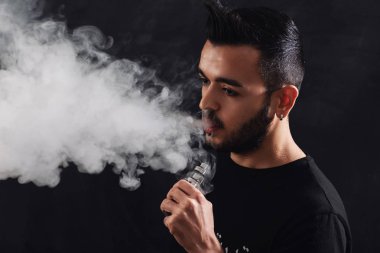 Siyah arka plan üzerinde elektronik sigara vaping sakallı genç adam.