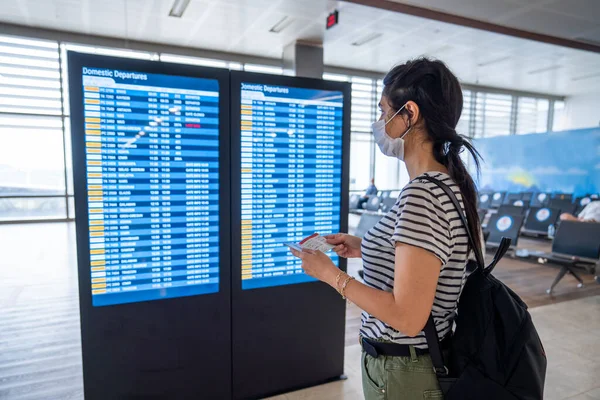 Young woman in virus protection face mask looking at information board in airport. Corona virus outbreaking. — Stock Photo, Image