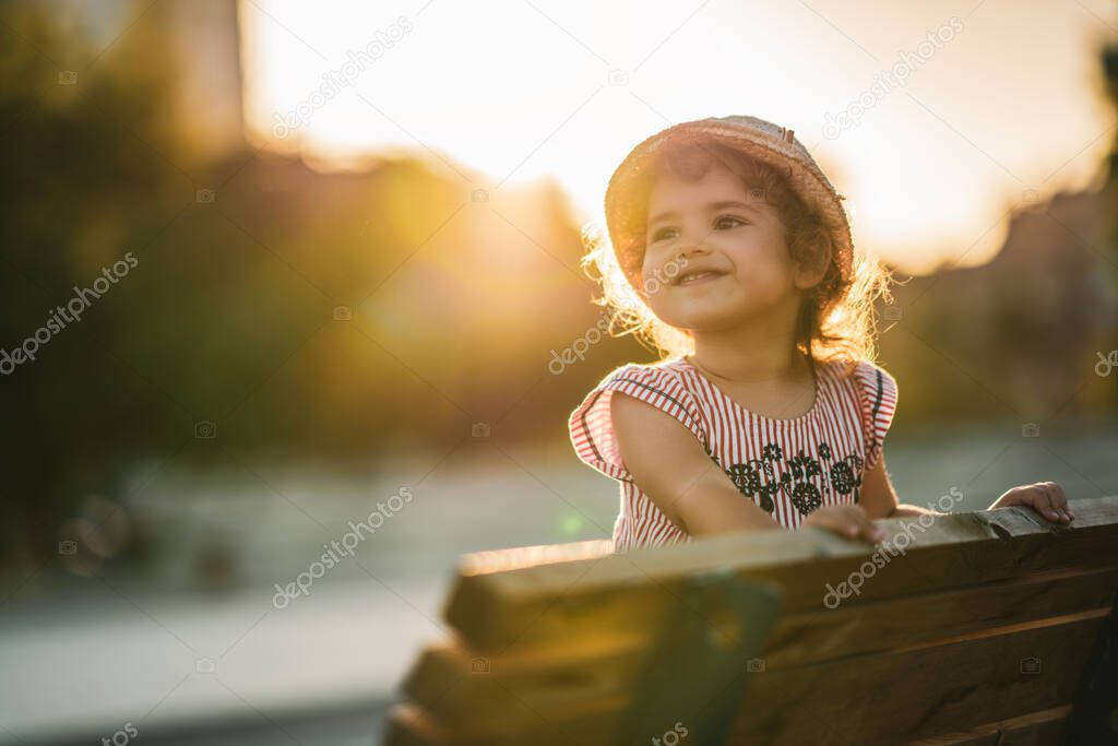 Portrait of a cute beautiful and happy girl standing on bench in the park