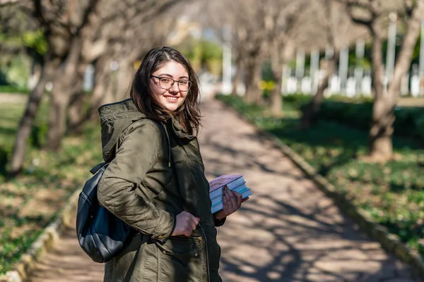 Chica joven intelectual se queda y mira a alguien en un parque con algunos libros en sus manos . — Foto de Stock