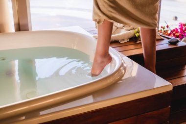 Kadın küvette banyo yapmak için suya ayağıyla dokunuyor.