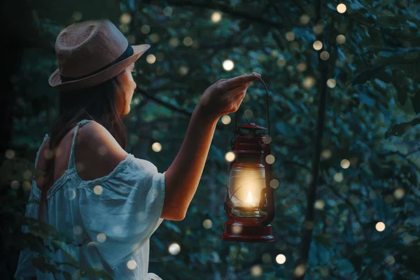Mulher bonita em vestido branco segurando uma lanterna em uma floresta com brilhos embaçados sob as árvores . — Fotografia de Stock