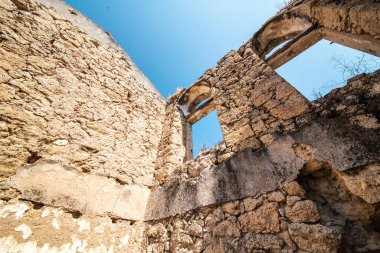 Mavi gökyüzünün altında taş duvarları olan eski yıkılmış ve terk edilmiş bir bina..