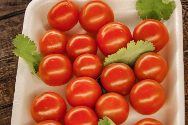 Tomates rojos cereza en un plato blanco con un fondo de madera — Foto de Stock