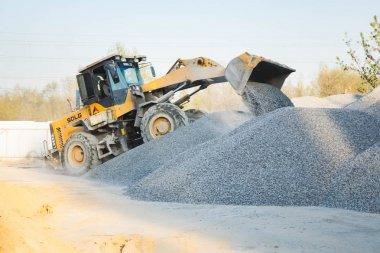 Voronej bölgesi, Rusya, 25 Nisan 2019. Traktör beton üretiminde ezilmiş taş yükler. Moloz yığınları halinde çalışan sarı traktör yükleyici. Kova beton yükler.