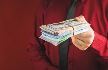 kırmızı bir arka plan üzerinde kırmızı takım elbiseli bir adamın elinde para tomarları