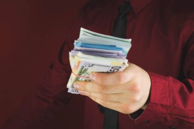 kırmızı bir arka plan üzerinde kırmızı takım elbiseli bir adamın elinde para tomarları