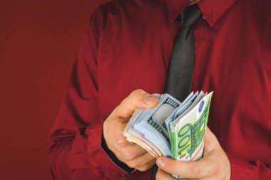 kırmızı bir arka plan üzerinde kırmızı takım elbiseli bir adamın elinde para tomarları