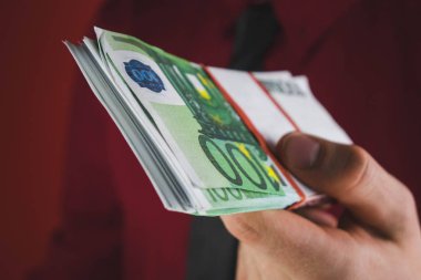 kırmızı takım elbiseli adam kırmızı arka plan üzerinde elinde para bir tomar tutar