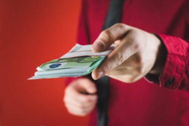 kırmızı takım elbiseli adam kırmızı arka plan üzerinde elinde para bir tomar tutar