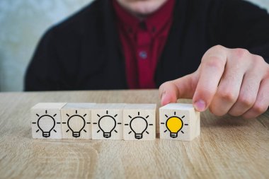 bir el, diğer tüm lambalar söndürüldüğünde yanan lambalı bir küp tutar, bu da Yeni Fikir'i, yenilik ve çözüm kavramlarını sembolize eder.